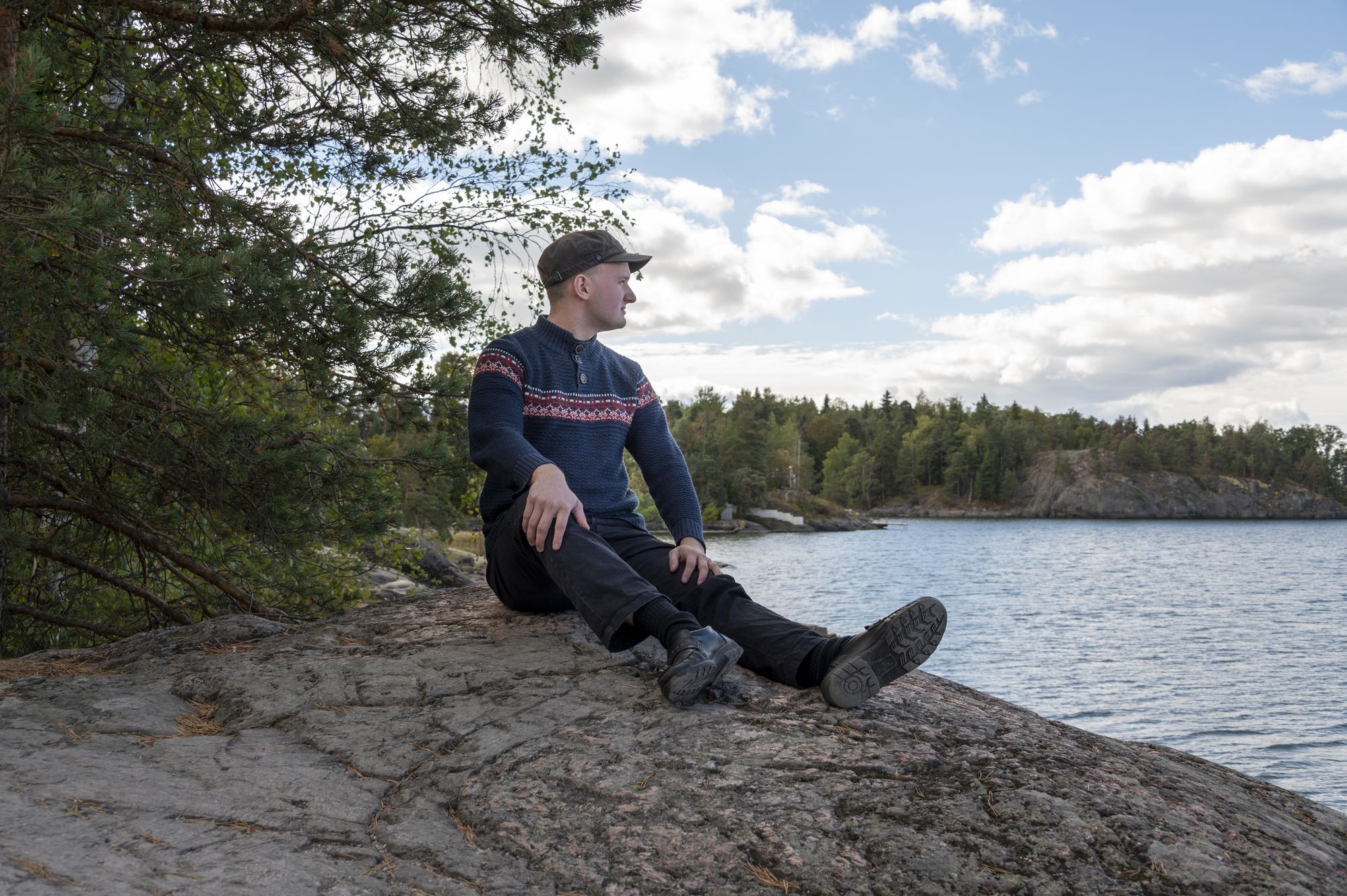 Santeri Leinonen istumassa kalliolla veden äärellä